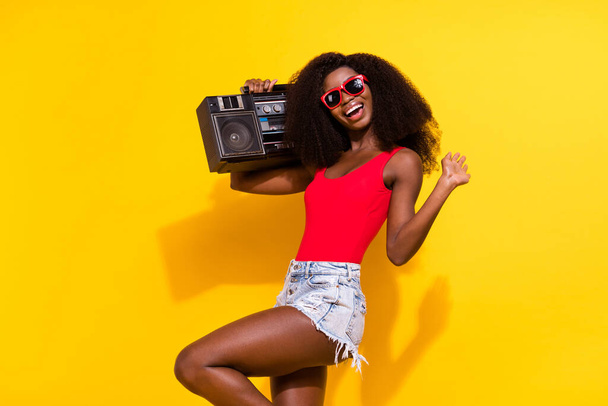Photo of charming nice dark skin woman hold boombox wear sunglass isolated on shine yellow color background. - Φωτογραφία, εικόνα