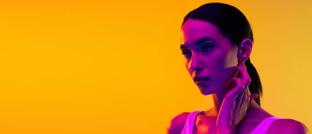 Portrait of beautiful young woman with low pony tail posing isolated over yellow studio background in neon light . Concept of beauty, body and skin care, sport, health, spa, cosmetics, ad. Flyer - Foto, imagen