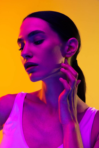 Portrait of tender young girl wit nude makeup and low pony rail posing isolated over yellow studio background in neon light. Concept of beauty, body and skin care, sport, health, spa, cosmetics, ad - Φωτογραφία, εικόνα