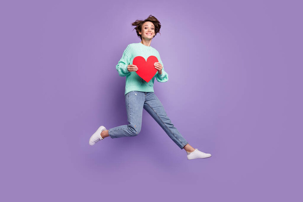 Full length body size photo of cheerful happy model jumping keeping red heart love symbol isolated pastel purple color background. - Zdjęcie, obraz