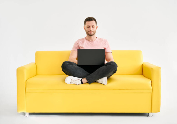 Uomo rilassato utilizzando computer portatile seduto su divano giallo su sfondo bianco. concetto di freelance - Foto, immagini