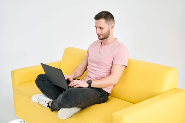 Relaxed man using laptop sitting on yellow sofa over white background. freelance concept - Foto, Imagen