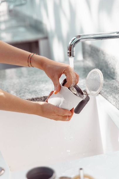 Hände einer Frau beim Reinigen der Teile einer Mokkakaffeemaschine unter einem Wasserstrahl - Foto, Bild