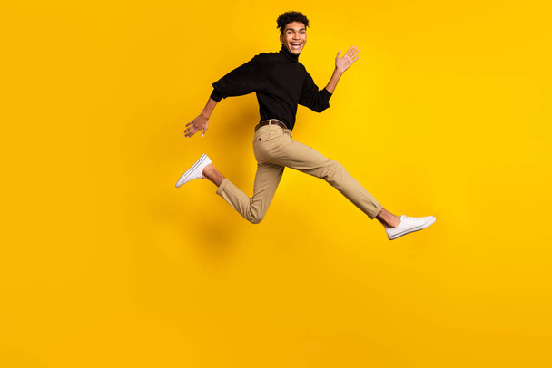 Photo of pretty charming dark skin man wear black sweater eyewear running fast jumping isolated yellow color background. - Fotó, kép