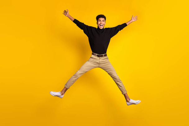 Photo of cute funny dark skin guy dressed black pullover jumping high like star isolated yellow color background. - Valokuva, kuva