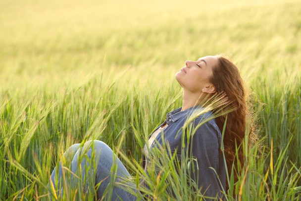 Side view portrait of a woman sitting in a wheat field breathing fresh air - Foto, Imagem