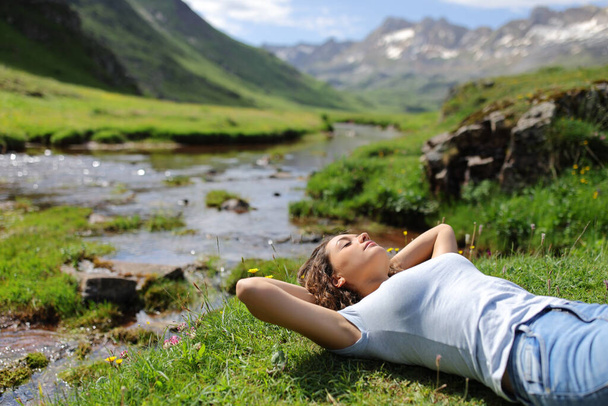 Woman resting and relaxing lying on the grass in a riverside in the mountain - Foto, immagini