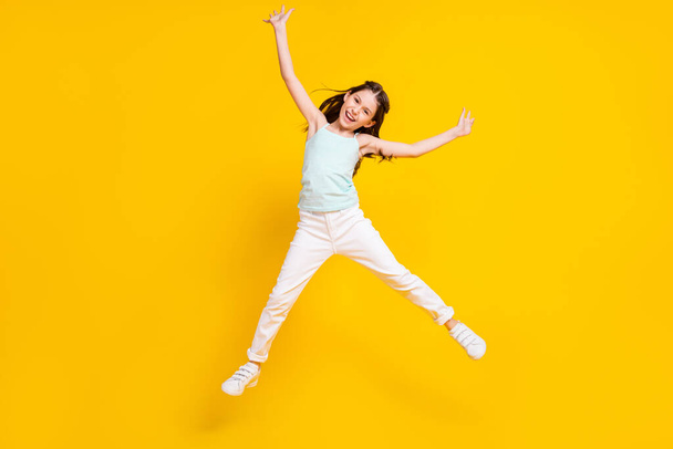 Full body photo of happy positive pretty little girl good mood raise hands jump isolated on yellow color background. - Foto, immagini