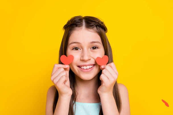 Photo of happy pretty cute little girl hold hands small red paper heart cheeks isolated on yellow color background. - Fotó, kép