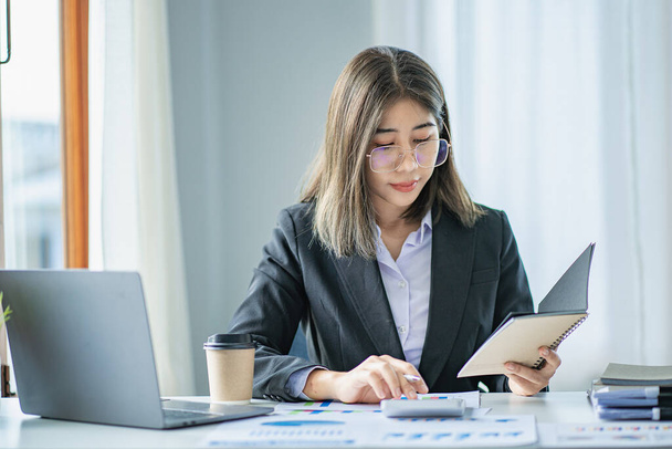 Empresária asiática trabalhando no escritório com papéis e segurando caneta usando laptop sentado na cadeira no estúdio doméstico moderno contato com os clientes - Foto, Imagem