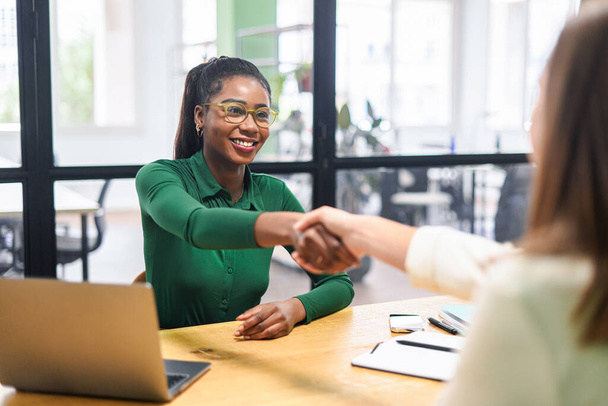 Business women shaking hands in the office during business meeting. Two diverse female entrepreneurs on meeting in boardroom. Female recruiter and employee confirm hiring - Fotó, kép