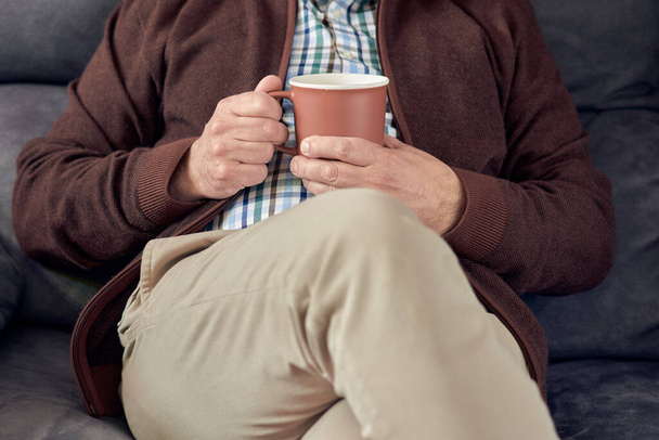 A man sitting on a sofa and enjoying a cup of tea - Фото, зображення