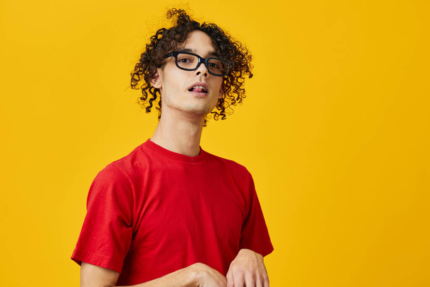 Funny cute myopic young student man in red t-shirt eyewear posing isolated on over yellow studio background. The best offer with free place for advertising. Education College concept - Photo, Image