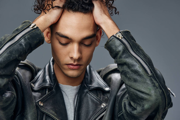 Portrait of stylish tanned curly man leather jacket touches head posing isolated on over gray studio background. Cool fashion offer. Huge Seasonal Sale New Collection concept. Copy space for ad - Fotoğraf, Görsel