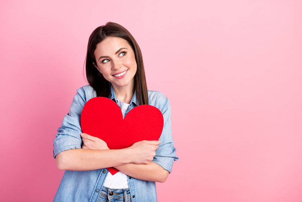 Photo of shiny adorable young lady wear denim shirt smiling hugging red hear looking empty space isolated pink color background. - 写真・画像