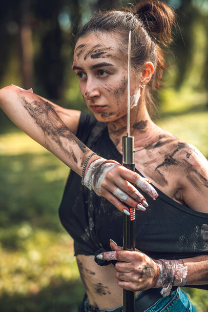 beautiful young girl in dirty ragged clothes with swords and knives in the woods trains. Concept of an armed girl in the woods - Fotoğraf, Görsel