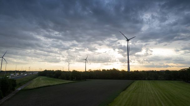 Panoramiczny widok z lotu ptaka na farmę wiatrową lub park wiatrowy, z wysokimi turbinami wiatrowymi do wytwarzania energii elektrycznej z przestrzenią kopiującą, przed dramatycznym zachodem słońca lub wschodem słońca z ciemnymi chmurami. Energia ekologiczna - Zdjęcie, obraz