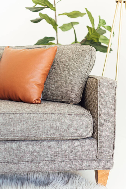 A vertical of a grey couch with a grey and a brown leather pillows on it in a living room - Photo, image
