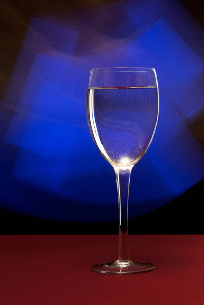 A vertical closeup of water in a wine glass against a blue neon light in a studio - Foto, afbeelding