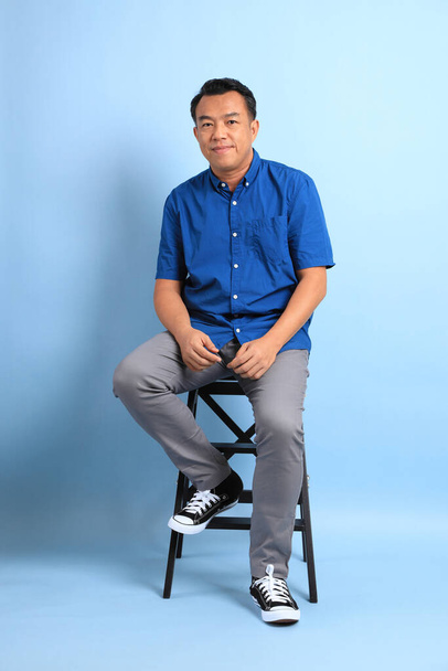 The Asian middle aged man with blue shirt sitting on the chair. - Foto, afbeelding