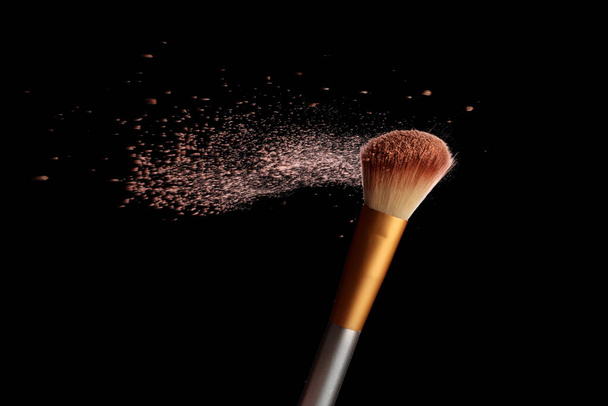 Maquillaje cepillo con salpicadura de polvo cosmético, sobre fondo negro. Imagen de salpicadura - Foto, imagen