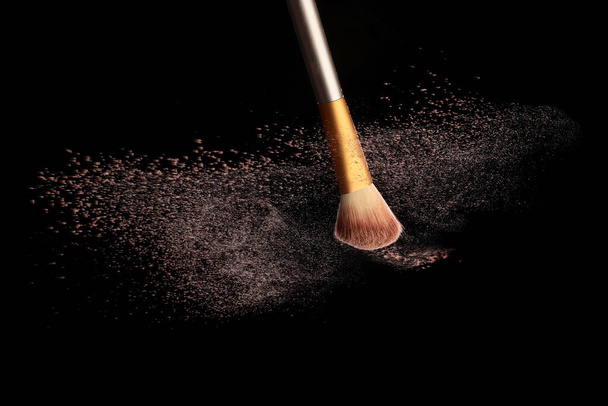 Maquillaje cepillo con salpicadura de polvo cosmético, sobre fondo negro. Imagen de salpicadura - Foto, Imagen