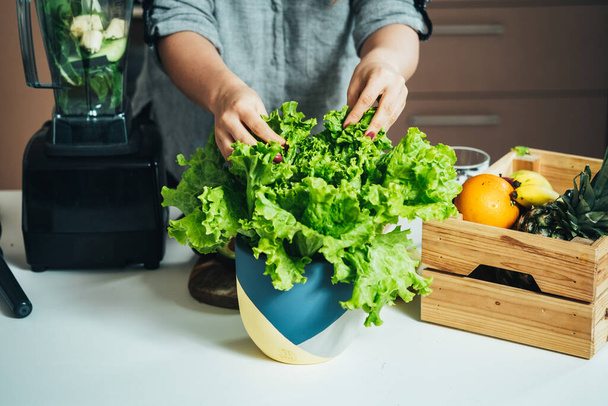 Nahaufnahme Foto von Frauenhänden, die frischen Salat nehmen und grünen Smoothie zum Frühstück zu Hause zubereiten - Foto, Bild