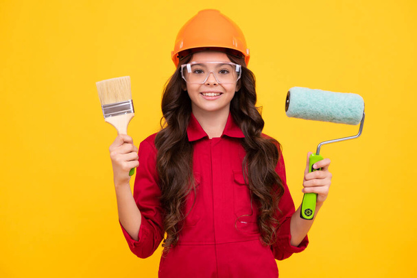 Painter in workshop. Renovation and repair. Teen girl in helmet with painting brush. Child in hard hat. Kid builder painter on construction site. Happy positive and smiling emotions of teenager girl - Foto, Imagem