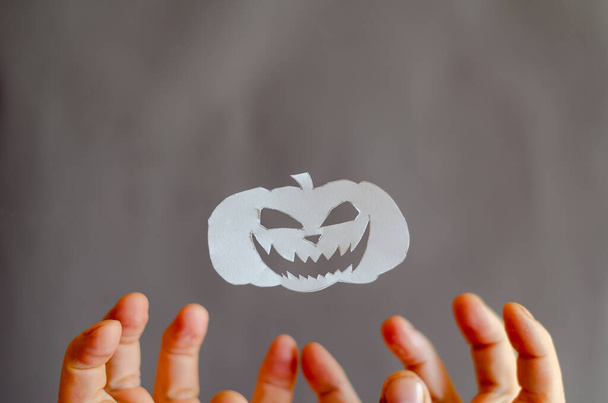 Biała księga Halloween Dynia i ręce z palcami zgiętymi w przerażeniu. Przedmioty halloweenowe pocięte nożyczkami z kartki papieru. Latanie w ir Silhouette Uśmiechnięta, onieśmielająca twarz. Ręce mężczyzny - Zdjęcie, obraz