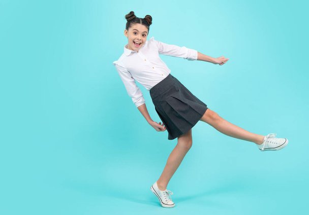 Happy schoolgirl, positive and smiling emotions of teen girl. Full length jump of teenager girl on blue isolated studio wear casual skirt and shirt. Funny school girl, amazed kid genius - Foto, Imagem