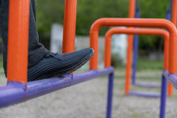 The lower section of a mature man engaged in restorative gymnastics on the sports ground. The man's legs are standing on the blue and orange bars. Recovery from a leg injury. Rehabilitation. Outside - Fotoğraf, Görsel