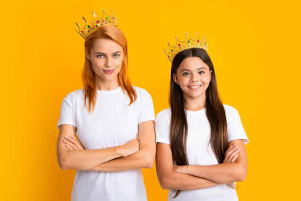 Arrogant mother and daughter child wearing crowns on yellow background, selfish. Studio portrait of teen princess - Zdjęcie, obraz