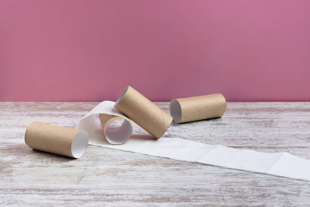 Empty cardboard toilet paper rolls. run out of perforated white toilet paper. The last piece of toilet paper. On a wooden table on a pink background - Foto, Imagen
