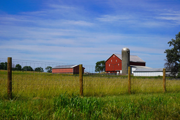 Ферма в Вирджинии с красным амбаром и зданиями, включая бункер. Линия ограждения проходит по полю. - Фото, изображение
