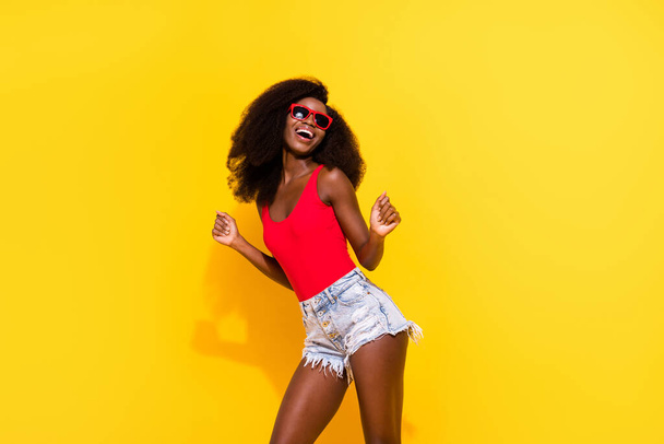 Photo portrait of dancing girl wearing red singlet shorts sunglass isolated bright yellow color background. - Foto, afbeelding