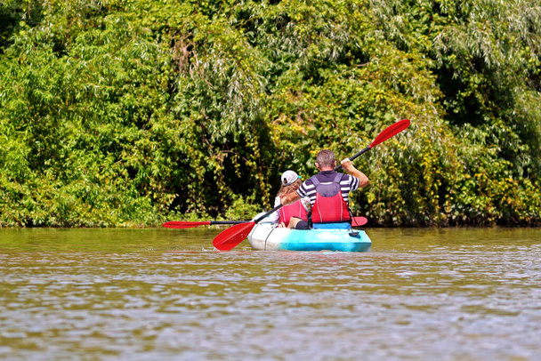 カヤックに乗っている少女と父親。父と子供は晴れた夏の日にドナウ川のカヤックで漕いでいます。休暇中のアクティブな水の楽しみ。カヤックツアーの家族. - 写真・画像