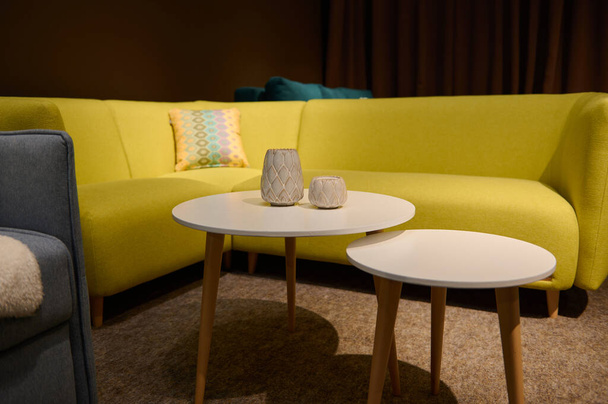 Удобный ярко-желтый диван с подушками в выставочном центре студии домашнего дизайна и круглый журнальный столик с каталогом. Дизайн интерьера и концепция улучшения дома - Фото, изображение
