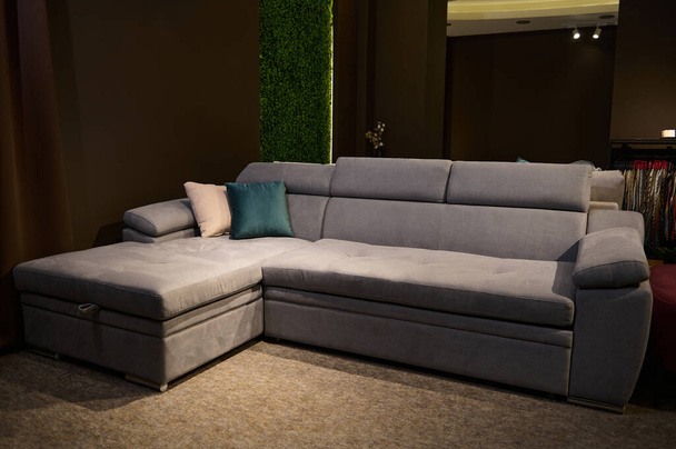 Elegante sofá gris con cojín verde y beige a la venta en la sala de exposición de muebles tapizados - Foto, imagen