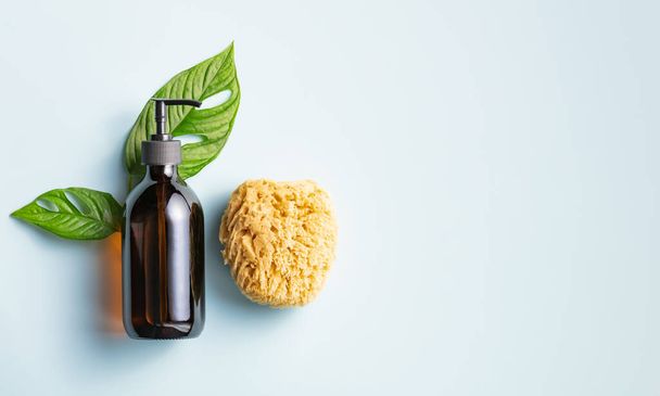 One cosmetic dark amber glass bottle with green plant and loofah on blue background. Closeup, copyspace. Beauty blog, salon treatment concept, minimalism brand packaging mock up - Fotografie, Obrázek
