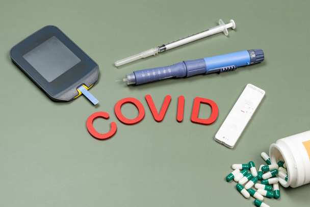 dispositivo para medir la glucosa en sangre, y la palabra Covid escrita en fondo verde, vista superior - Foto, Imagen