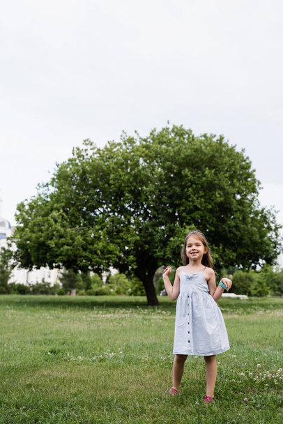 Gelukkig emotioneel kind meisje poseert buiten in het groene park. Mode jongen. Glimlachend poedelmeisje lopend in het park - Foto, afbeelding