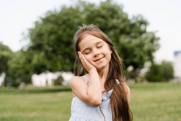 Tender toddler child girl touching her cheek and smile. Adorable kid posing outside in the park - 写真・画像
