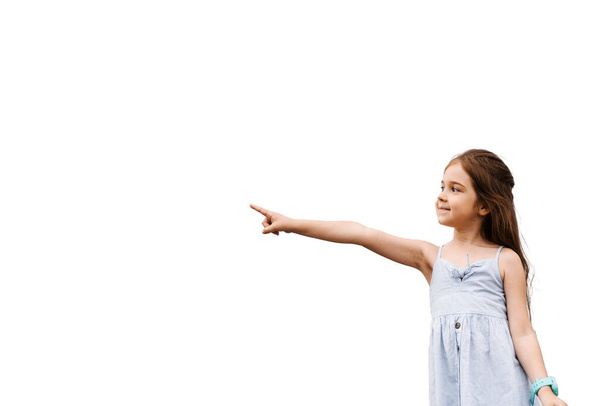 Adorable niña apuntando con el dedo a la izquierda sobre fondo blanco con espacio en blanco para el anuncio. Idea creativa para la venta de descuento para productos para niños - Foto, Imagen