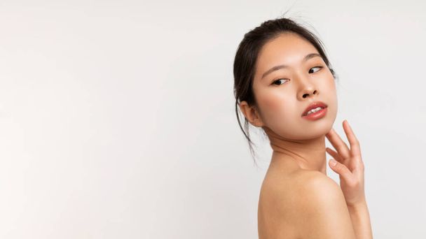 Arcápolási koncepció. Portré fiatal érzéki ázsiai hölgy néz vissza másolás tér felett fehér stúdió háttér, megérinti az arcát, panoráma fénymásolás hely - Fotó, kép