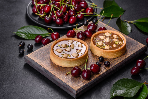 Delicious fresh nougat and nut tart with fresh berries on a wooden cutting board against a dark concrete background - Photo, Image