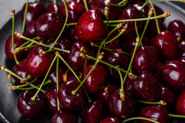 Fresh red cherries fruit on a plate on a dark concrete background. Close up - Photo, Image