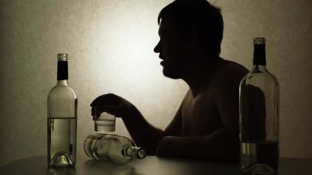 Alkoholik pijący wódkę siedzący przy stole z butelkami, sylwetka wideo. - Materiał filmowy, wideo