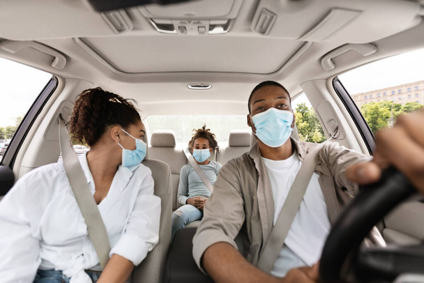 3人乗りのアフリカ系アメリカ人家族は車の中で座ります,コヴィト-19防止のための保護顔マスクを身に着けています.自動車旅行の安全性と保険の概念。選択的フォーカス - 写真・画像