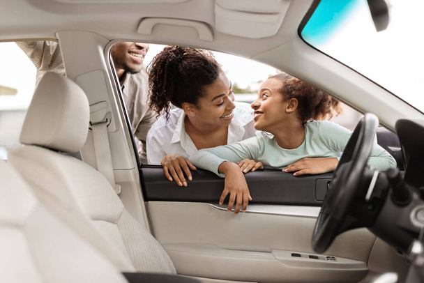 Concesionario de coches. Alegre familia afroamericana de tres vehículos de elección mirando a través de la ventana en el interior del automóvil. Auto Leasing Business Concept. Enfoque selectivo - Foto, imagen