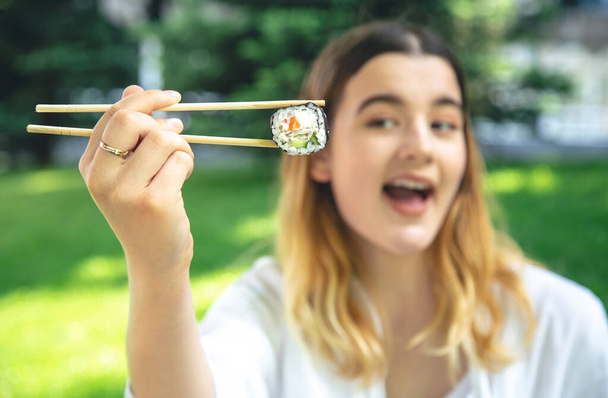 Jovem atraente comendo sushi na natureza, piquenique de verão, rolos maki. - Foto, Imagem